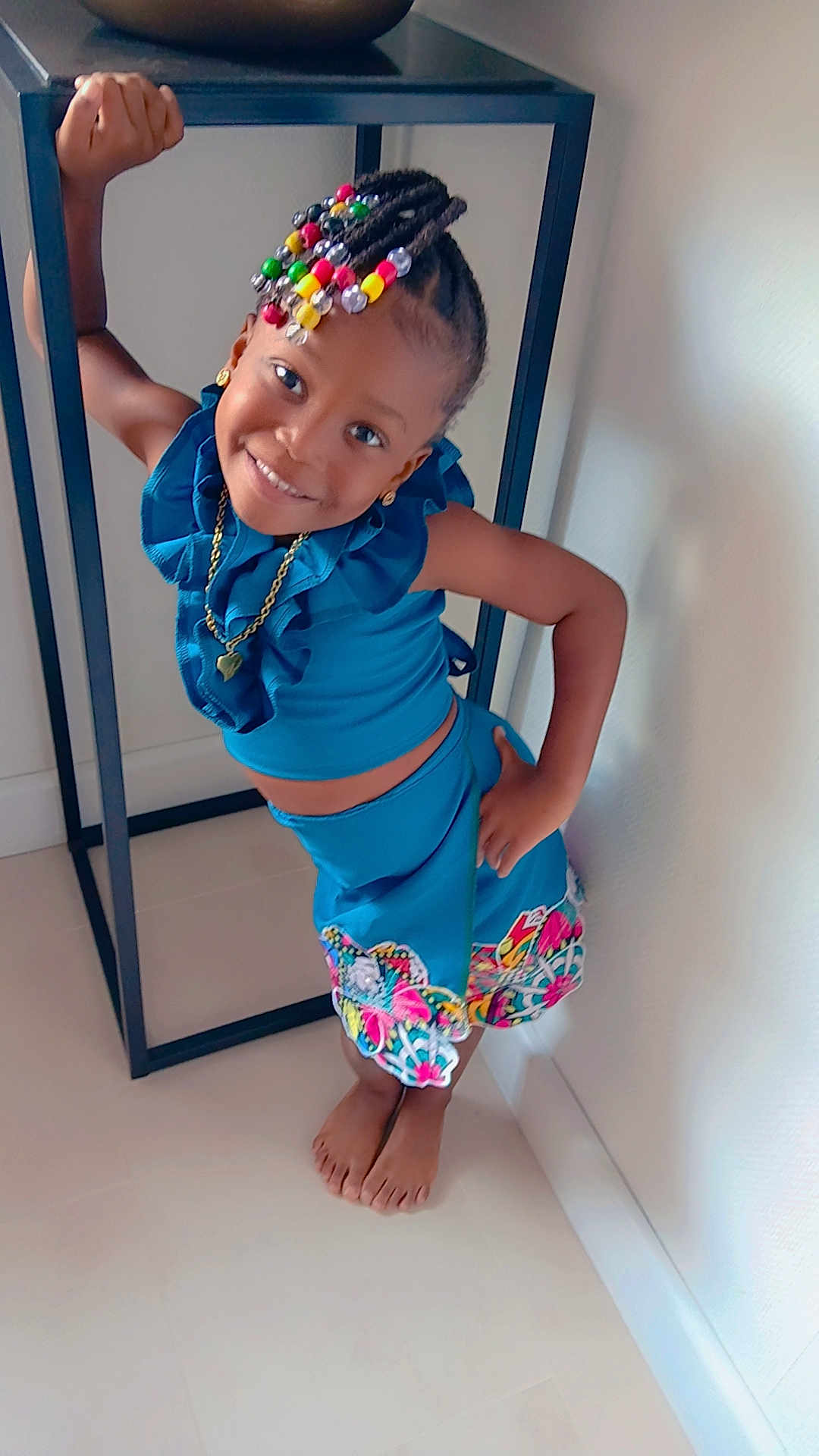 Melyanna a rejoint le concours — aidez-le/la à gagner de superbes lots ! child, girl, smile, pose, indoor, blue_outfit, braids, colorful_beads, barefoot, floor, wall, table, jewelry, necklace, earrings, happy, portrait, fashion, cute, playful