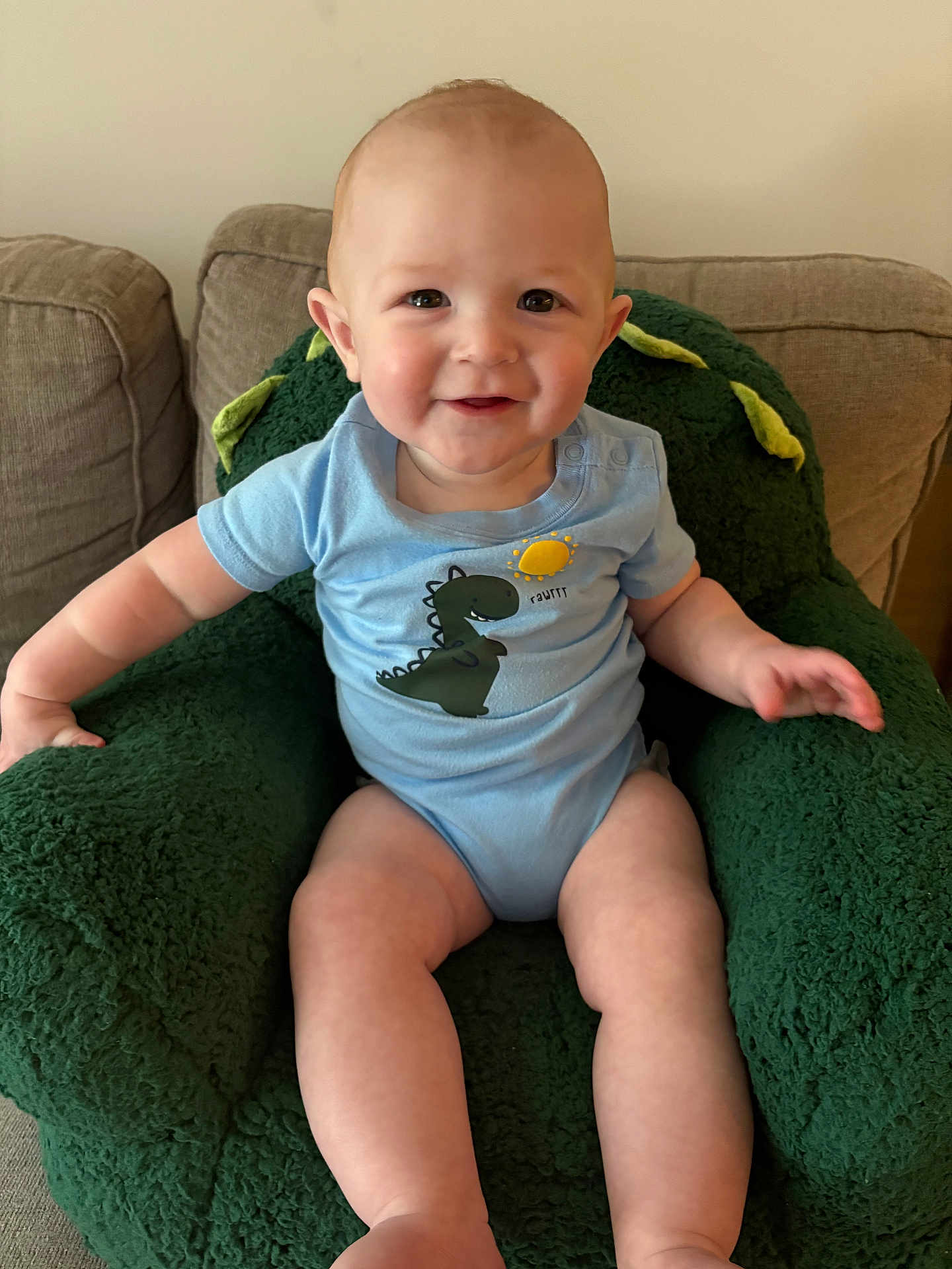 Cameron joined the competition — help win amazing prizes! baby, child, onesie, dinosaur, smile, green_chair, plush_chair, indoor, couch, happy, cute, toddler, person, seated, furniture, cozy, infant, portrait, home, comfort