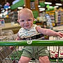 baby, child, shopping_cart, grocery_store, smile, striped_shirt, green_shorts, seatbelt, shopping, aisle, store, cute, happy, person, infant, retail, playful, tongue_out, indoor, young_child