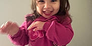 Isabella is registered to the contest to win money with this photo: toddler, child, smiling, pink_sweatshirt, indoor, carpet, wall, cartoon_characters, motion_blur, happy, person, clothing, long_hair, playful, cute, young_child, standing, casual_wear, expression, portrait