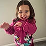 toddler, child, smiling, pink_sweatshirt, indoor, carpet, wall, cartoon_characters, motion_blur, happy, person, clothing, long_hair, playful, cute, young_child, standing, casual_wear, expression, portrait