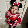 toddler, child, costume, minnie_mouse, red_dress, polka_dots, bow, headband, ears, indoor, floor, door, security_camera, black_shoes, curly_hair, cute, looking_up, portrait, person, standing