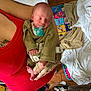 arm, baby, blanket, casual, clothing, floor, footwear, hand, household_items, indoors, infant, newborn, pacifier, person, play_mat, red_clothing, resting, sleeping, tattoo, wooden_floor