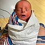 Colton is registered to the contest to win money with this photo: baby, blanket, closed_eyes, face, floor, head, indoor, infant, lap, newborn, peaceful, person, ripped_jeans, skin, sleeping, small, striped_blanket, swaddled, tattoo, wood_floor