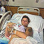 hospital_bed, mother, newborn, baby, hospital_room, medical_equipment, tattoo, blanket, woman, patient, bed, pillow, striped_blanket, hospital, postpartum, infant, healthcare, rest, skin, person