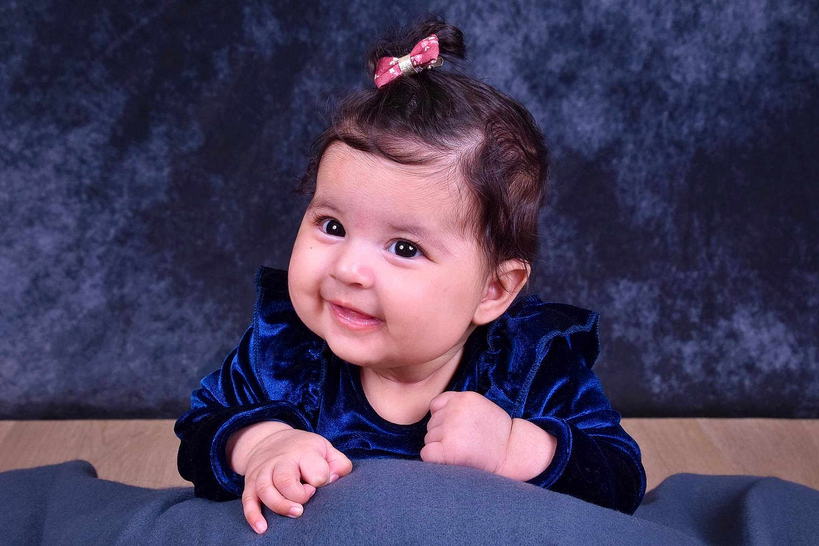 Amira Naima a rejoint le concours — aidez-le/la à gagner de superbes lots ! adorable, baby, child, cushion, cute, dark_background, face, hands, happy, head, indoor, infant, person, pink_bow, portrait, smiling, soft_toy, studio_photo, velvet_clothing, young_child