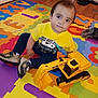 Yael De Leon is registered to the contest to win money with this photo: child, toddler, toy, excavator, yellow_shirt, colorful_mat, foam_puzzle, indoor, flooring, sneakers, playtime, wood_floor, room, doorway, wall, cable, clothing, person, smile, young_child