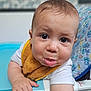 Maé a rejoint le concours — aidez-le/la à gagner de superbes lots ! baby, child, infant, high_chair, bib, white_shirt, curious_eyes, puckered_lips, chubby_cheeks, hand, face, indoor, furniture, patterned_cushion, close_up, cute, expression, skin, person, portrait
