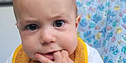 Maé participe au concours pour gagner de l'argent avec cette photo : baby, child, face, hand, fingers, teething, bib, clothing, highchair, indoor, expression, curious, skin, portrait, closeup, infant, cute, person, young, colorful_background