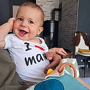 Maé participe au concours pour gagner de l'argent avec cette photo : baby, child, smiling, happy, indoor, person, toy, shirt, text, hand, face, head, furniture, brick_wall, chair, adult, holding, colorful, cute, portrait