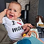 baby, child, smiling, happy, indoor, person, toy, shirt, text, hand, face, head, furniture, brick_wall, chair, adult, holding, colorful, cute, portrait
