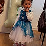 bag, balloon, birthday, blue_dress, celebration, chair, child, curly_hair, dress, floor, indoor, number_one, party, plant, slippers, spoon, toddler, white_tights, white_wall, wooden_floor