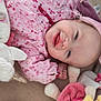 baby, smiling, pink_clothing, plush_toy, hat, lying_down, cute, child, soft_toys, face, happy, infant, indoors, portrait, fabric, hand, headwear, cozy, playful, closeup