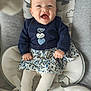 baby, smiling, infant, clothing, sitting, baby_seat, patterned_skirt, navy_top, heart_design, white_tights, happy, indoors, child, cute, portrait, furniture, cushion, young_child, face, hands