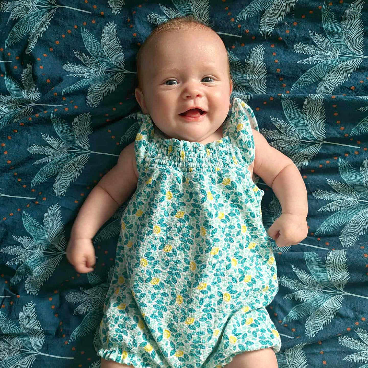 Lyana participe au concours pour gagner de l'argent avec cette photo : arms, baby, blanket, child, clothing, cute, expression, face, happy, indoors, infant, leaf_pattern, legs, lying_down, person, portrait, romper, skin, smiling, young