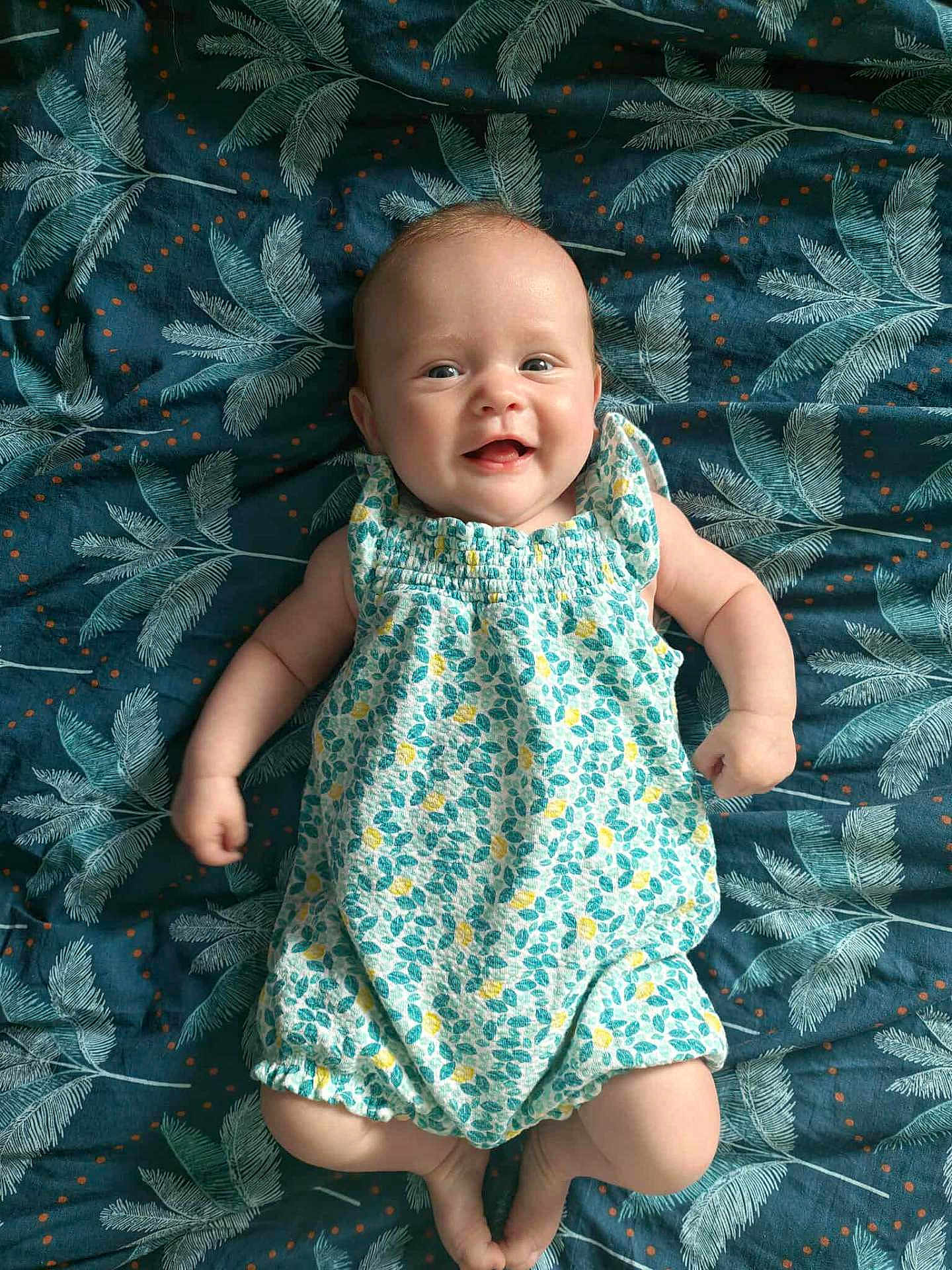 Lyana participe au concours pour gagner de l'argent avec cette photo : baby, infant, smiling, romper, leaf_pattern, blanket, happy, lying_down, cute, child, skin, face, arms, legs, clothing, indoors, portrait, young, person, expression