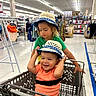 Leo joined the competition — help win amazing prizes! baby, child, clothing, department_store, family, green_shirt, happy, indoor, matching_hats, orange_shirt, portrait, retail, shopping, shopping_cart, siblings, sitting, smiling, sun_hat, supermarket, toddler