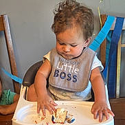 Leo is registered to the contest to win money with this photo: baby, bib, birthday, brown_hair, cake, celebration, child, curly_hair, eating, food, high_chair, indoor, messy, party, portrait, serious, smiling, streamers, table, toddler