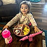 breakfast, child, couch, dessert, dining_table, food, girl, highchair, home, indoors, living_room, portrait, scrambled_eggs, sippy_cup, smiling, sprinkles, tablet, toddler, toy, wood_floor