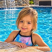 Ellie is registered to the contest to win money with this photo: child, girl, swimming_pool, swimmer, smiling, portrait, outdoor, summer, water, waterfall, wet_hair, swimsuit, poolside, sunlight, backyard, stone, fountain, relaxation, happy, vacation