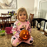 Ellie is registered to the contest to win money with this photo: cartoon_clothing, chairs, child, countertop, dining_room, dining_table, family_home, flowers, girl, halloween, high_chair, indoor, jack_o_lantern, kitchen, pajamas, pink, portrait, pumpkin, smiling, toddler