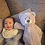 Legend is registered to the contest to win money with this photo: baby, teddy_bear, plush_toy, couch, cushion, smiling, infant, striped_clothing, bib, indoor, soft_toy, happy, child, cozy, furniture, portrait, cute, relaxing, home, person