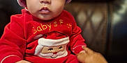 Legend joined the competition — help win amazing prizes! baby, child, santa_hat, red_clothing, holiday_outfit, christmas, cute, wide_eyes, indoor, leather_chair, hand, sitting, portrait, face, expression, festive, warm, cozy, infant, person