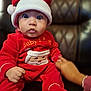 baby, child, santa_hat, red_clothing, holiday_outfit, christmas, cute, wide_eyes, indoor, leather_chair, hand, sitting, portrait, face, expression, festive, warm, cozy, infant, person