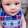 baby, child, face, blue_eyes, plaid_clothing, red, white, blue, american_flag, star_pattern, infant, cute, portrait, closeup, smiling, skin, hand, cushion, seated, fashion