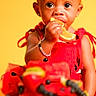 blueberries, bracelet, celebration, child, closeup, curious, cute, food, fruit_cake, happy, orange_slice, portrait, red_dress, sitting, snack, summer, sweet, toddler, vibrant_colors, yellow_background
