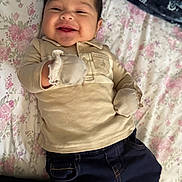 Carlos is registered to the contest to win money with this photo: baby, infant, smiling, mittens, clothing, bedspread, floral_pattern, happy, person, portrait, laying_down, cute, young_child, indoor, fabric, comfort, casual_wear, head, face, child