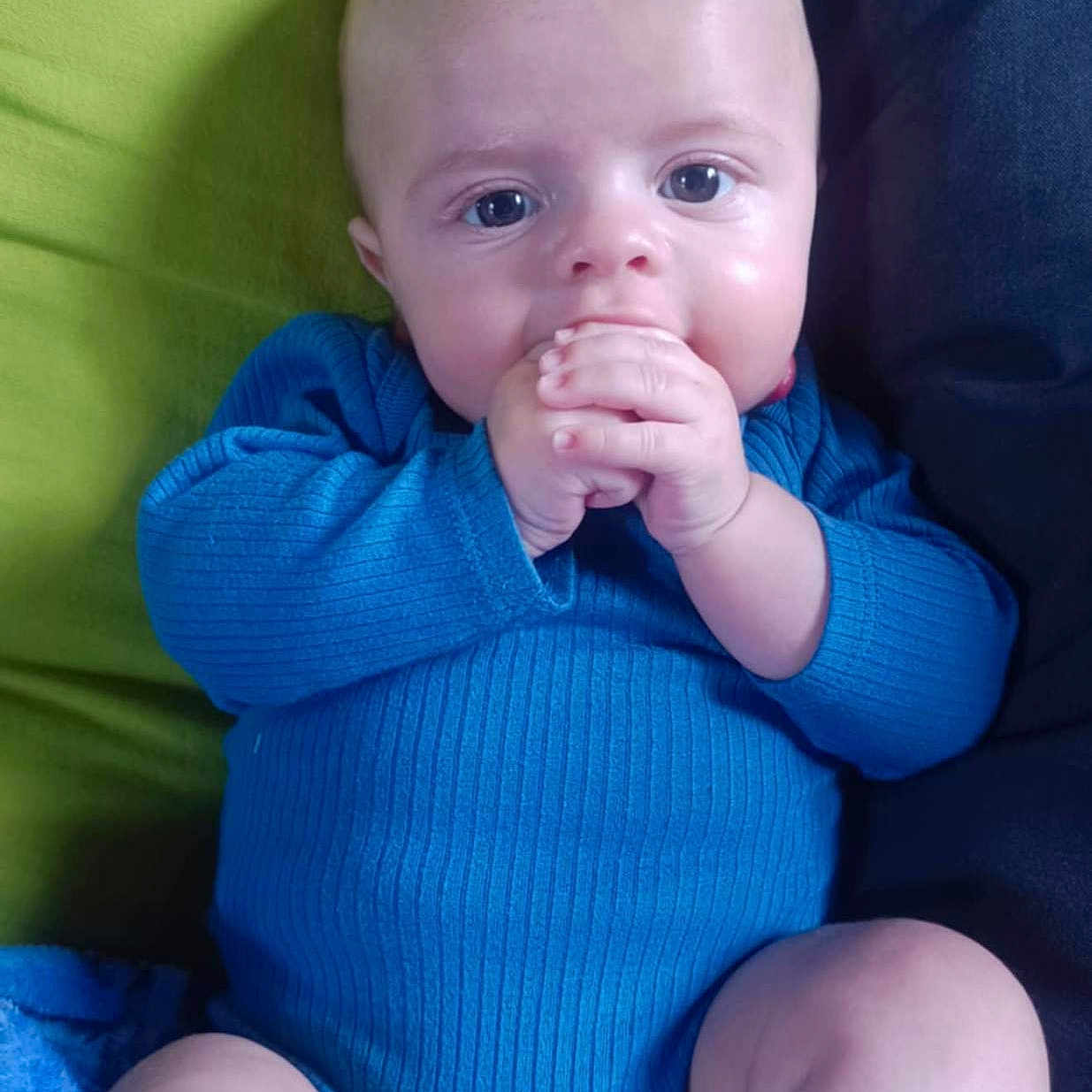 Liam participe au concours pour gagner de l'argent avec cette photo : baby, blue_onesie, child, closeup, comfort, cushion, cute, dark_background, eyes, face, green_background, hands, indoor, infant, legs, person, portrait, sitting, skin, young
