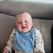 Oscar joined the competition — help win amazing prizes! baby, smiling, sitting, blue_bib, white_outfit, teddy_bear_prints, couch, gray_couch, happy, infant, cute, child, indoor, portrait, young_child, face, hands, clothing, soft_lighting, home