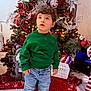 child, christmas_tree, curious, decorations, festive, floor, gift_box, green_sweater, holiday, holiday_decor, indoor, jeans, lights, ornaments, seasonal, sneakers, standing, toddler, winter_clothing, young_child