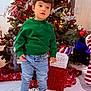 celebration, child, christmas_tree, curly_hair, cute, festive, floor, gift_boxes, green_sweater, holiday_decor, holiday_spirit, indoor, jeans, lights, ornaments, shoes, standing, toddler, winter_clothes, young_child