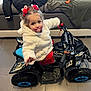 child, toddler, toy, quad_bike, indoor, floor, couch, jacket, pacifier, hair_accessories, red, white, black, blue, smiling, person, furniture, play, young_child, cute