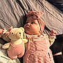 baby, infant, pink_clothing, headband, plush_toy, teddy_bear, bed, blanket, soft_toy, child, cute, portrait, indoor, person, sleepwear, fabric, hand, face, cozy, resting