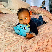 Roderick is registered to the contest to win money with this photo: baby, infant, child, plush_toy, octopus_toy, bed, bedding, pillow, blanket, indoor, portrait, lying_down, crawling, smiling, onesie, cute, lamp, window, curtains, nursery