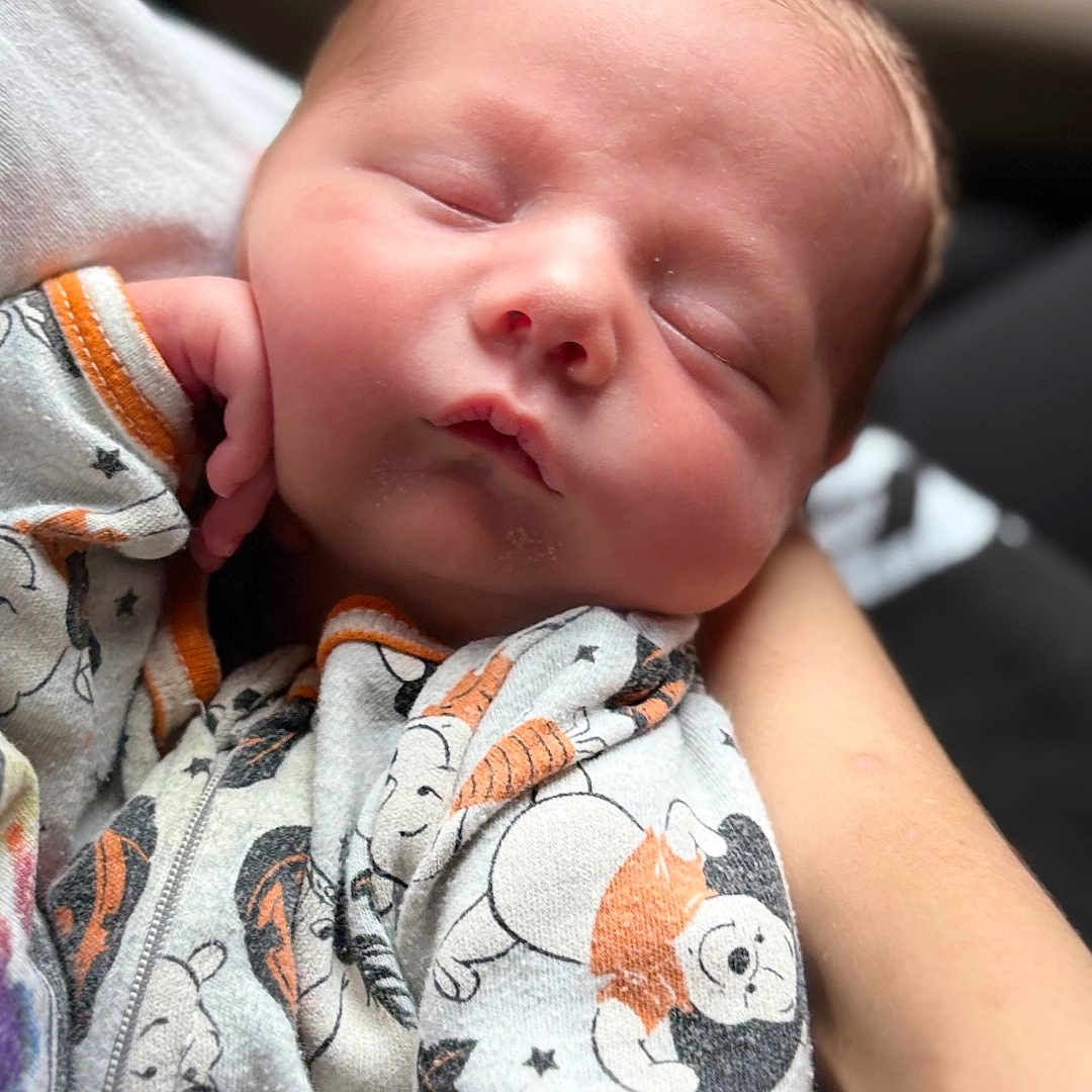 Kaden is registered to the contest to win money with this photo: newborn, baby, sleeping, onesie, cartoon_characters, infant, peaceful, closeup, hand, soft_light, portrait, cute, child, person, cozy, resting, baby_clothes, newborn_baby, sleep, holding