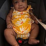 baby, child, car_seat, yellow_clothing, onesie, bow, infant, seatbelt, cute, smiling, indoors, sitting, young_child, face, skin, foot, hand, straps, safety, portrait