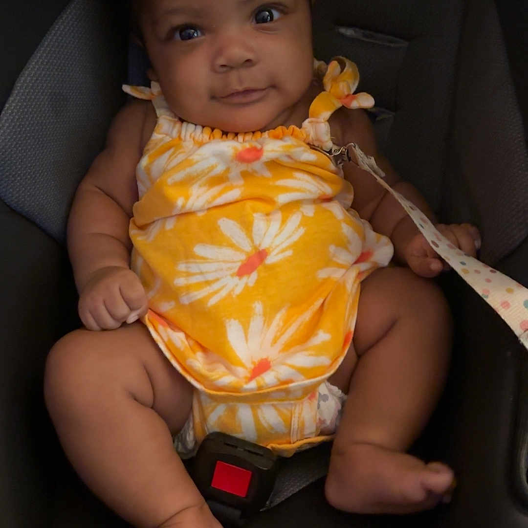 Alaia joined the competition — help win amazing prizes! baby, bow, car_seat, child, cute, face, foot, hand, indoors, infant, onesie, portrait, safety, seatbelt, sitting, skin, smiling, straps, yellow_clothing, young_child