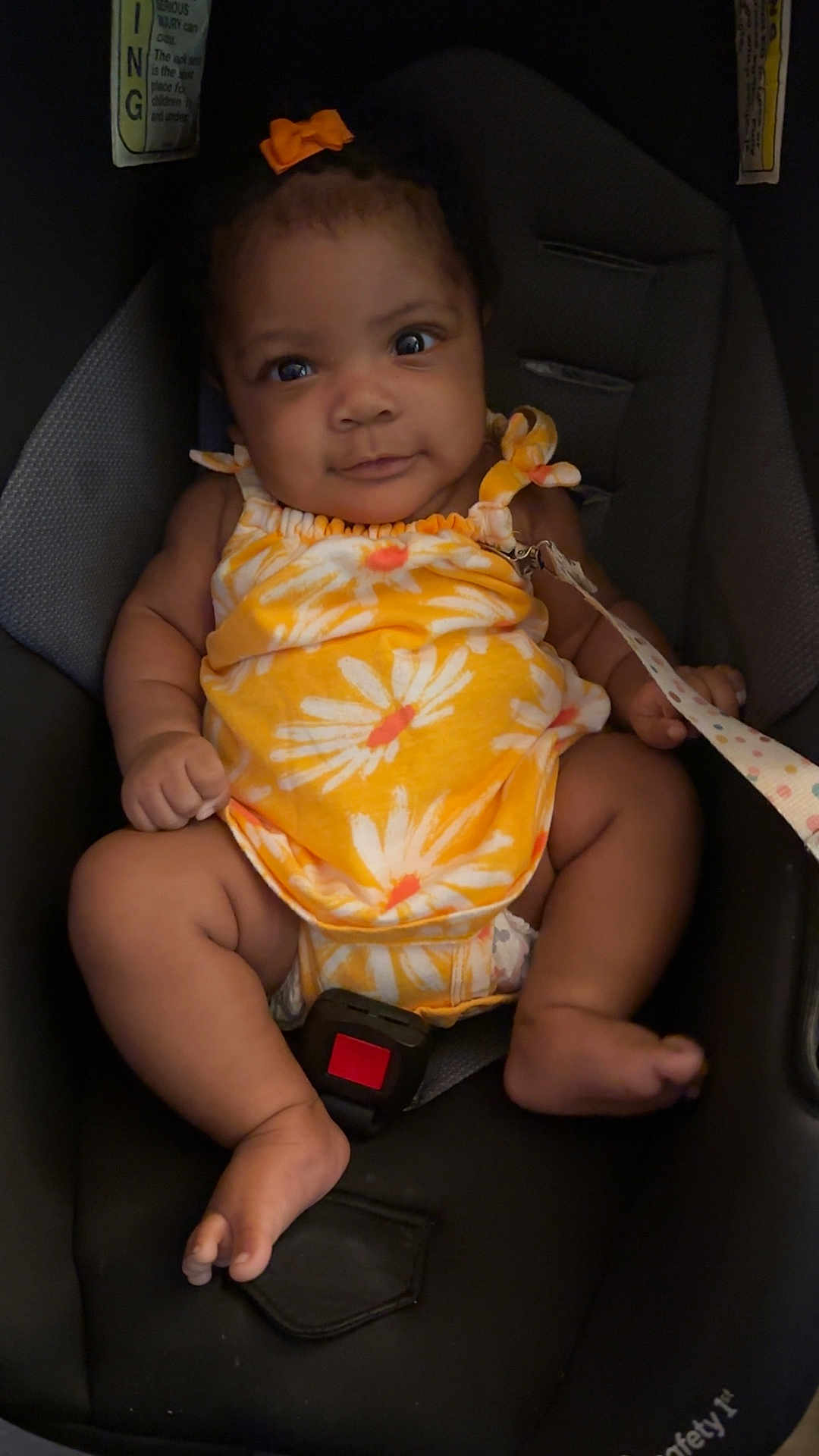 Alaia joined the competition — help win amazing prizes! baby, child, car_seat, yellow_clothing, onesie, bow, infant, seatbelt, cute, smiling, indoors, sitting, young_child, face, skin, foot, hand, straps, safety, portrait