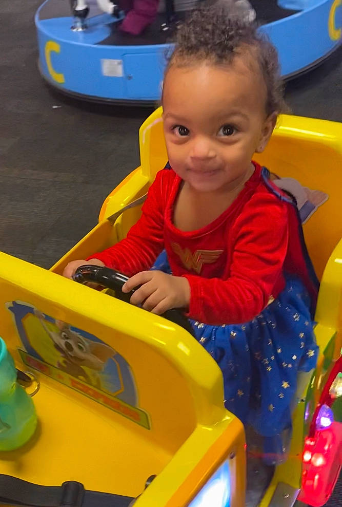 Cassidy is registered to the contest to win money with this photo: amusement_ride, blue, child, electric_blue, engineering, fun, human_settlement, leisure, motor_vehicle, outdoor_recreation, person, play, playground, recreation, riding_toy, sitting, smile, toddler, vehicle, wheel