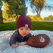 Callahan is registered to the contest to win money with this photo: baby, infant, beanie, hat, football, outdoor, grass, quilt, blanket, tree, sunset, child, cute, portrait, nature, greenery, daylight, crawling, face, expression