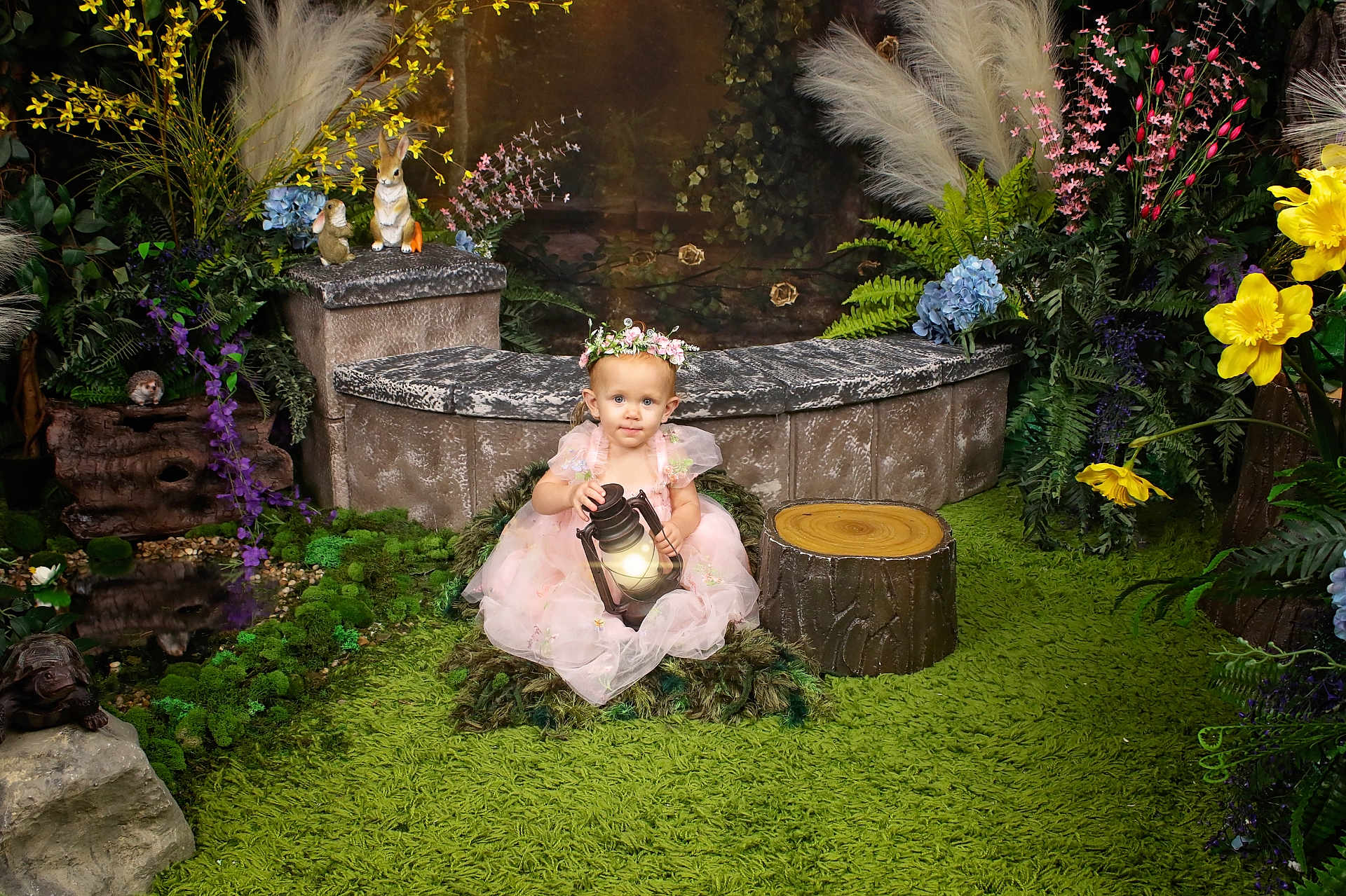 Valerie joined the competition — help win amazing prizes! toddler, child, lantern, pink_dress, flower_crown, green_rug, artificial_flowers, foliage, garden_scene, decorative_animals, rabbit_figurine, hedgehog_figurine, tree_stump, bench, portrait, indoor, whimsical, fairy_tale, cute, sitting