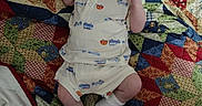 Owen is registered to the contest to win money with this photo: baby, infant, pacifier, quilt, blanket, colorful, pattern, clothing, white_shoes, footwear, lying_down, indoor, child, cute, person, fabric, textile, soft, small, looking