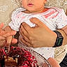 adult, baby, birthday, cake, cap, child, chocolate, hands, hat, holding, indoor, infant, onesie, party, pink_clothing, portrait, smartwatch, smiling, table, wide_eyed
