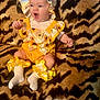 Annabella is registered to the contest to win money with this photo: baby, bonnet, child, clothing, comfort, cute, expression, headwear, indoor, infant, legs, mouth_open, patterned_blanket, portrait, ruffled_socks, sitting, sunflower_pattern, tiger_striped_blanket, white_socks, yellow_outfit