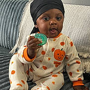 Dakari is registered to the contest to win money with this photo: baby, child, pajamas, pumpkin, headwrap, pacifier, couch, blue_couch, plush, smiling_face, cute, infant, sitting, hand, footed_pajamas, orange, white, indoor, cozy, portrait