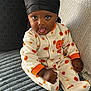Dakari is registered to the contest to win money with this photo: baby, child, infant, onesie, pumpkin_pattern, black_durag, tongue_out, couch, pillow, cozy, smiling, cute, indoor, portrait, sitting, happy, home, soft_texture, clothing, person